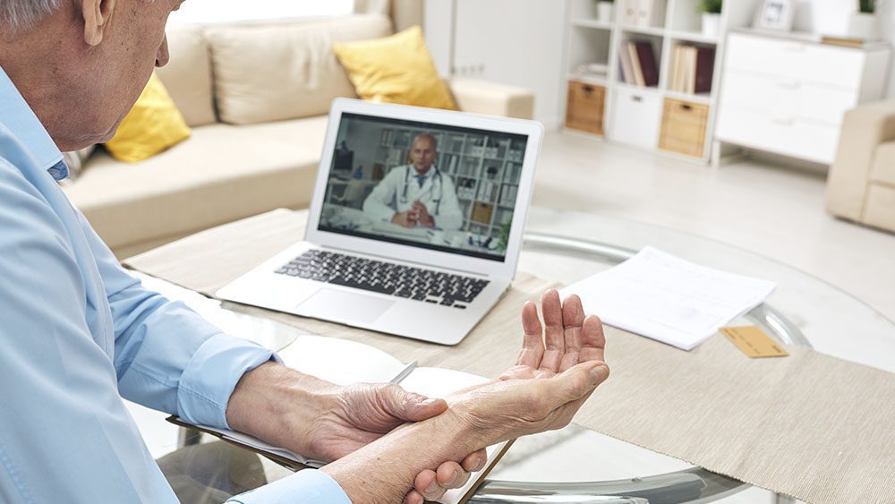 Patient on telemedicine video call with doctor. Patient is holding their wrist or checking pulse