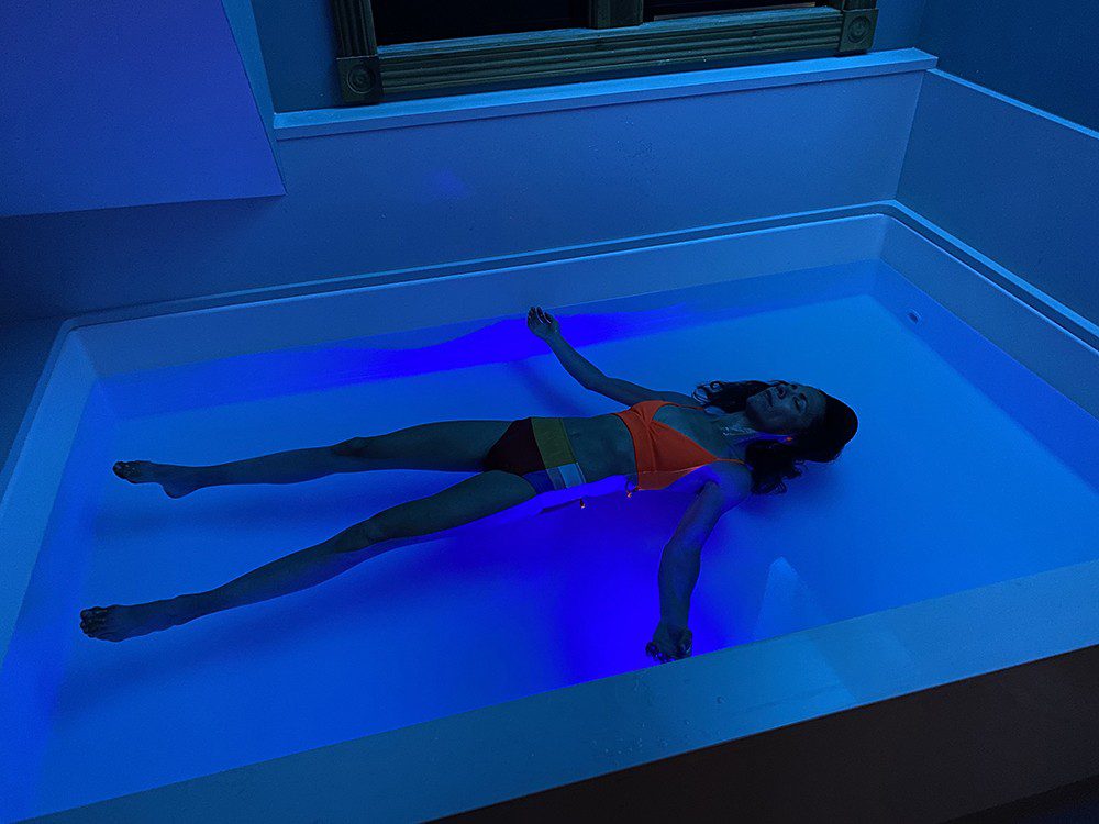 Person floating in a float tank. Dark room with minimal purple light