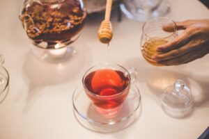Scooping honey into a glass cup of red tea. 