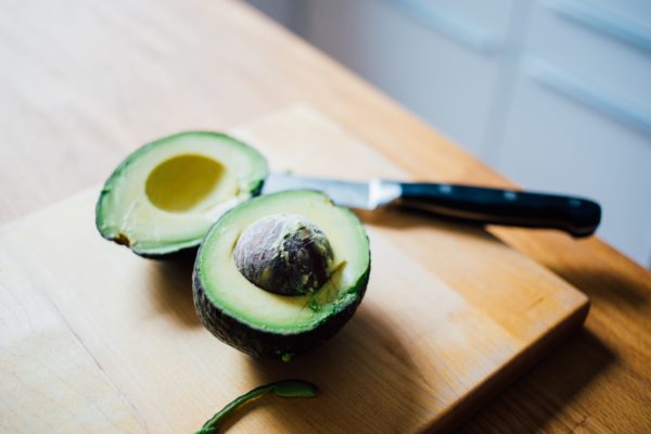 Halved avocado with pit still attached on wooden cutting board next to knife