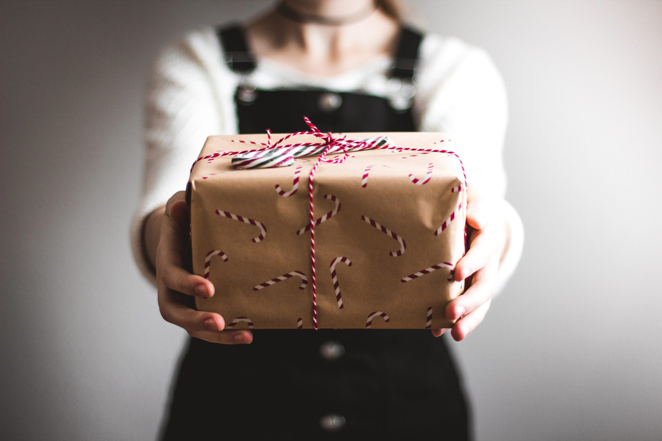 Person holding wrapped gift out in front of them. Brown paper wrapping paper with red and white candy canes