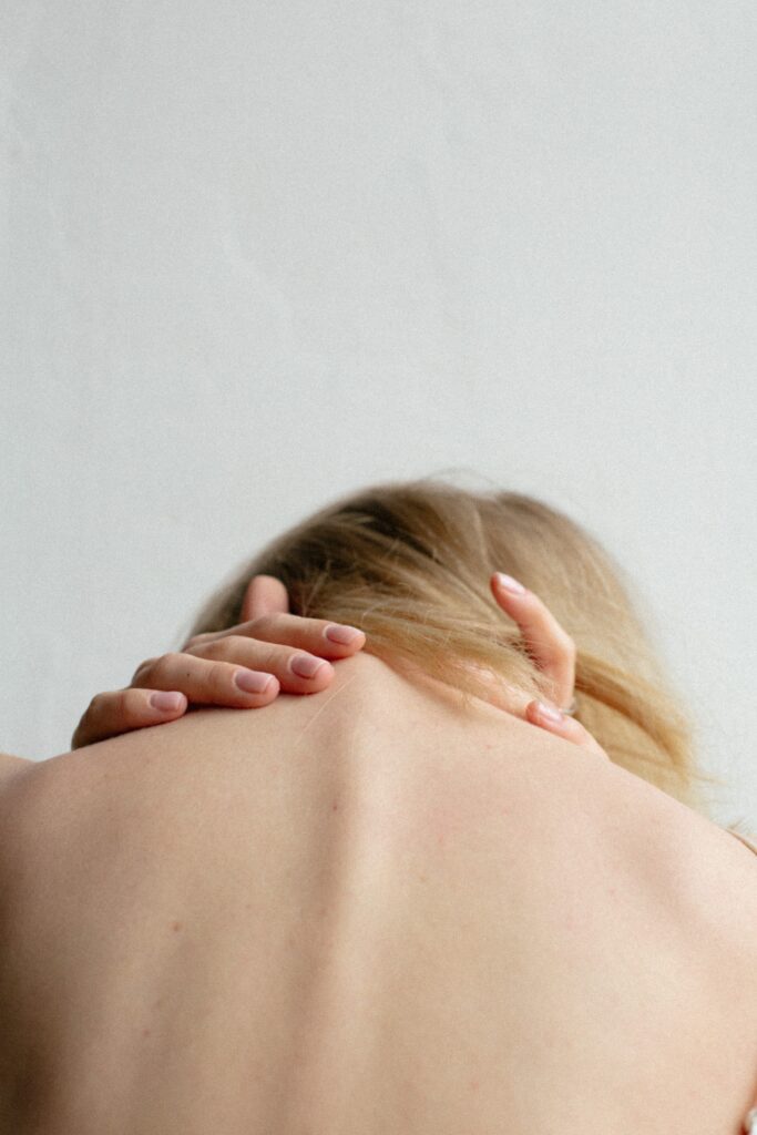 woman grabbing back of neck in pain, can see spine and back of head pictured