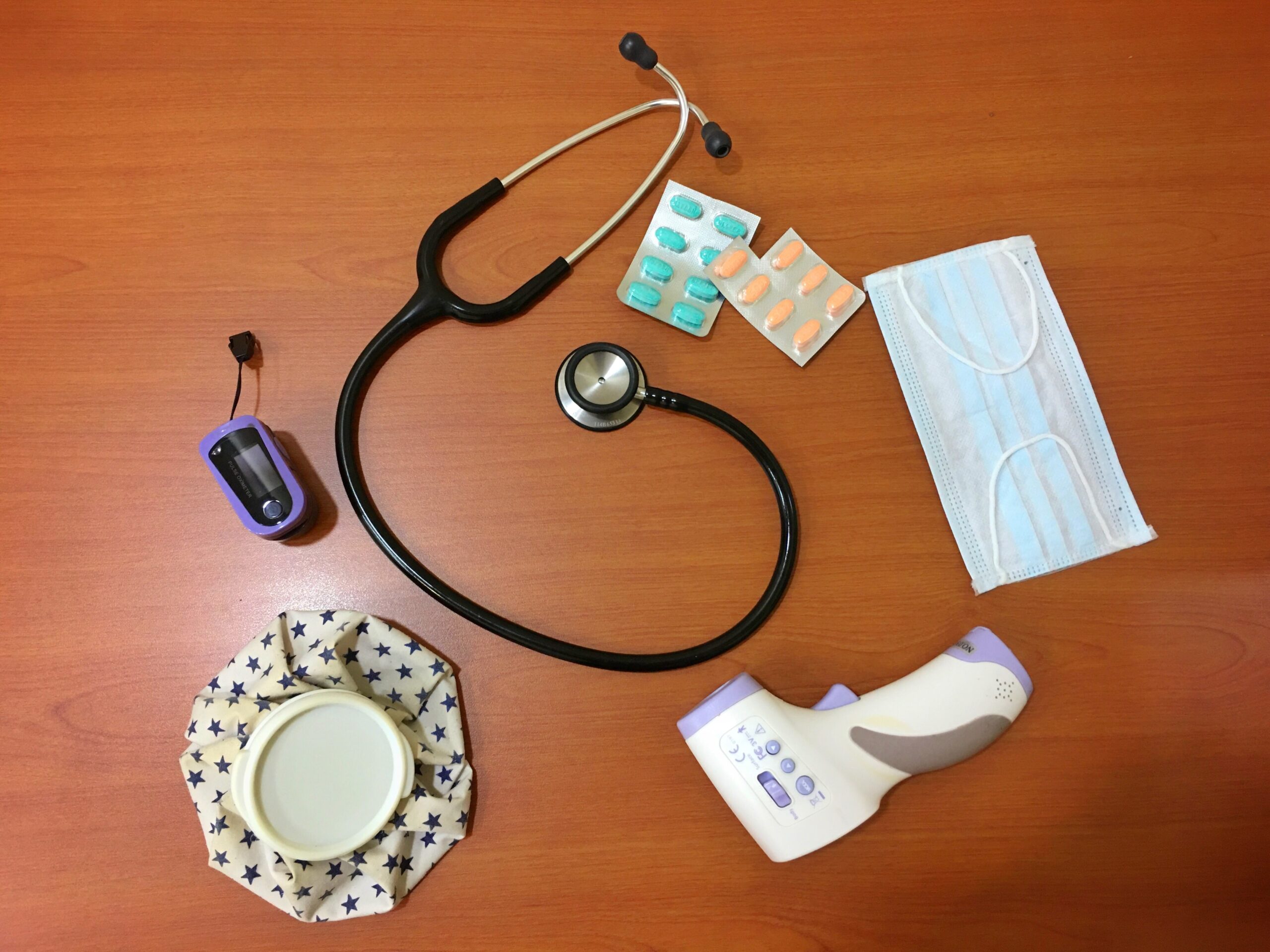 stethoscope, thermometer, surgical mask, and supplements on a wooden surface