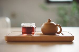 Glass of red tea next to a brown, ceramic teapot