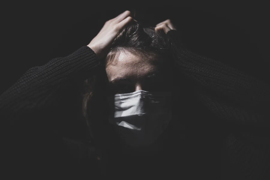 Person wearing surgical mask clenching their hair in their hands. Very dark photo