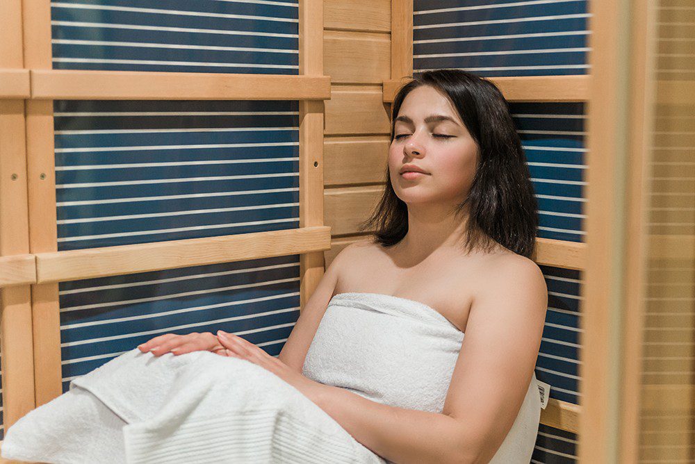 Young woman relaxing in a sauna dressed in a towel. Infrared panels and wooden walls