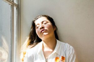 Woman sitting with eyes closed in sunlight. Exhausted, Lack of sleep 