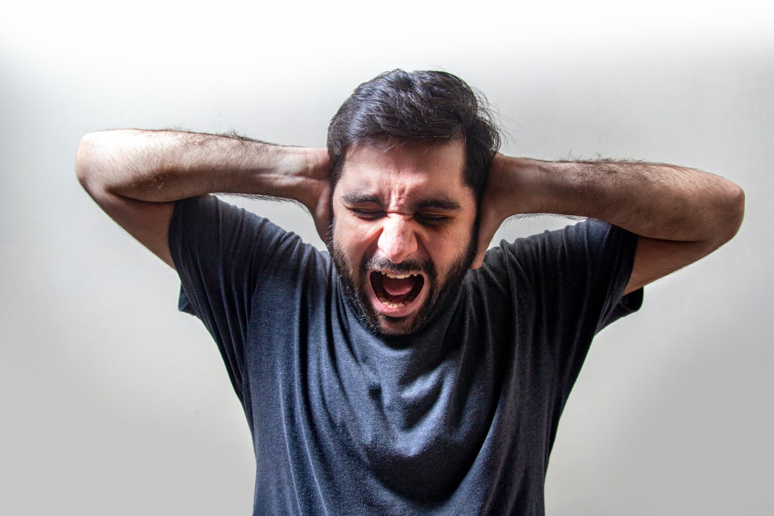 man holding both of his hands up to each side of his head. He is making a rage screaming face in anger