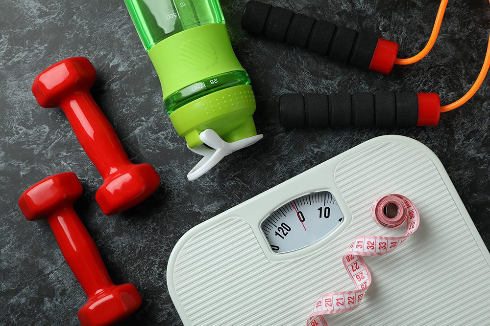 Scale, dumbbells, jumprope, water bottle, and tape measure against gray background