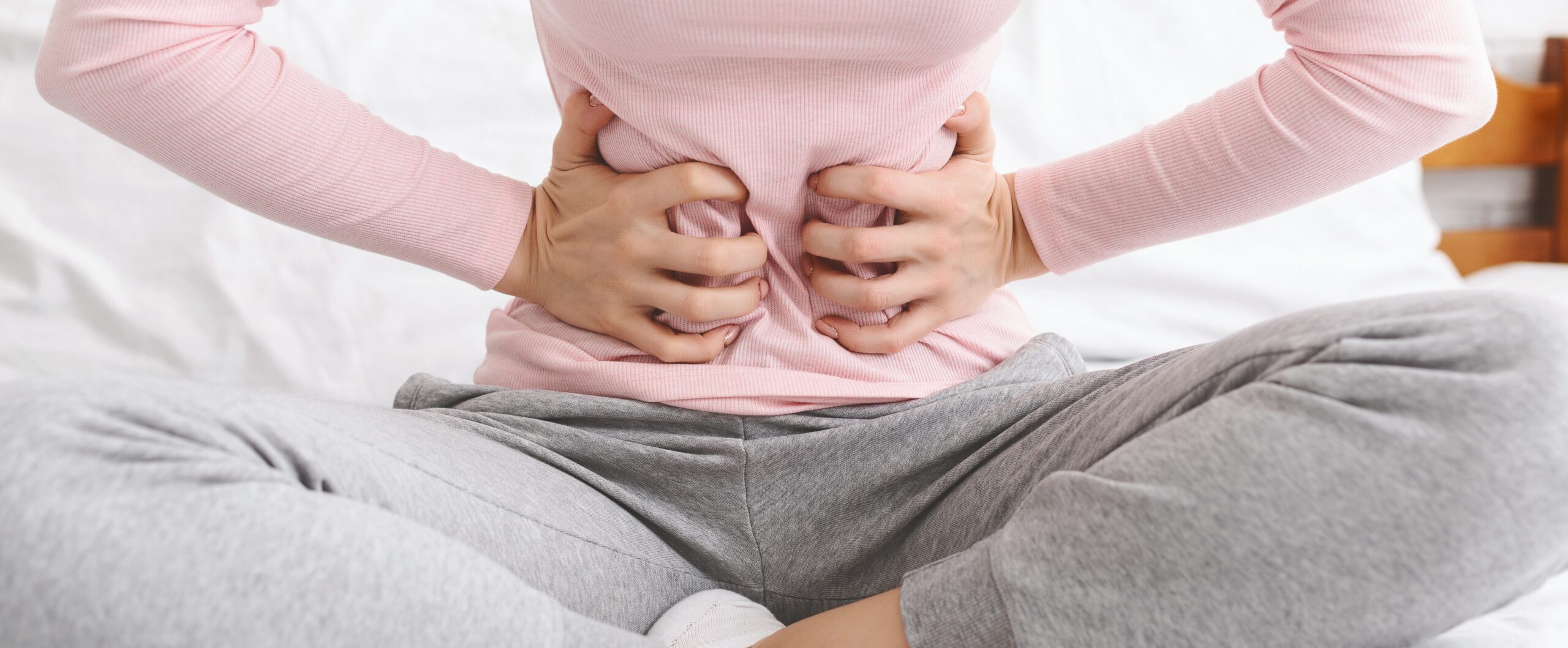 Person suffering from cramps or stomach pain. They are holding their abdomen in pain while sitting cross legged