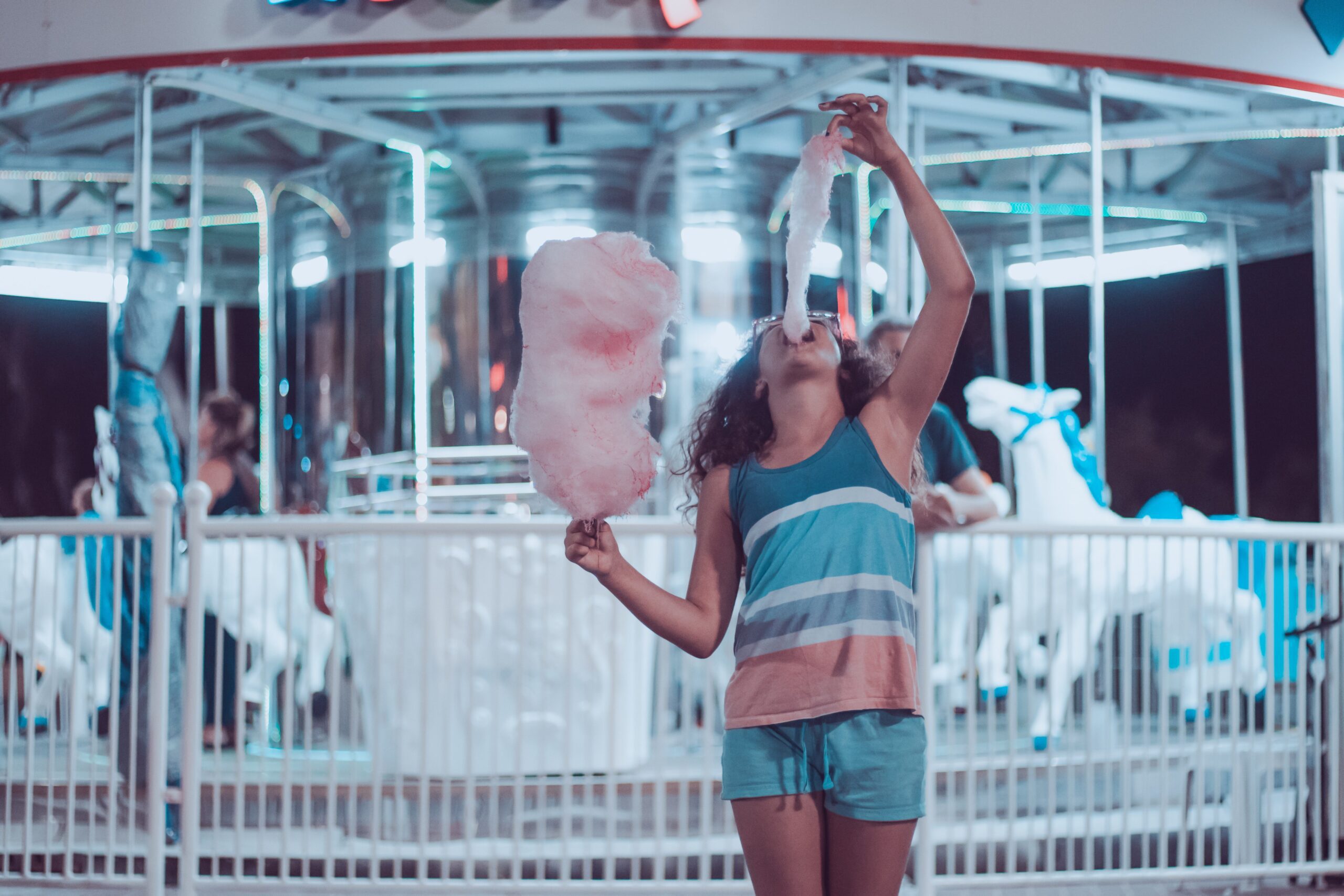 sugar Person standing in front of carousel while eating cotton candy